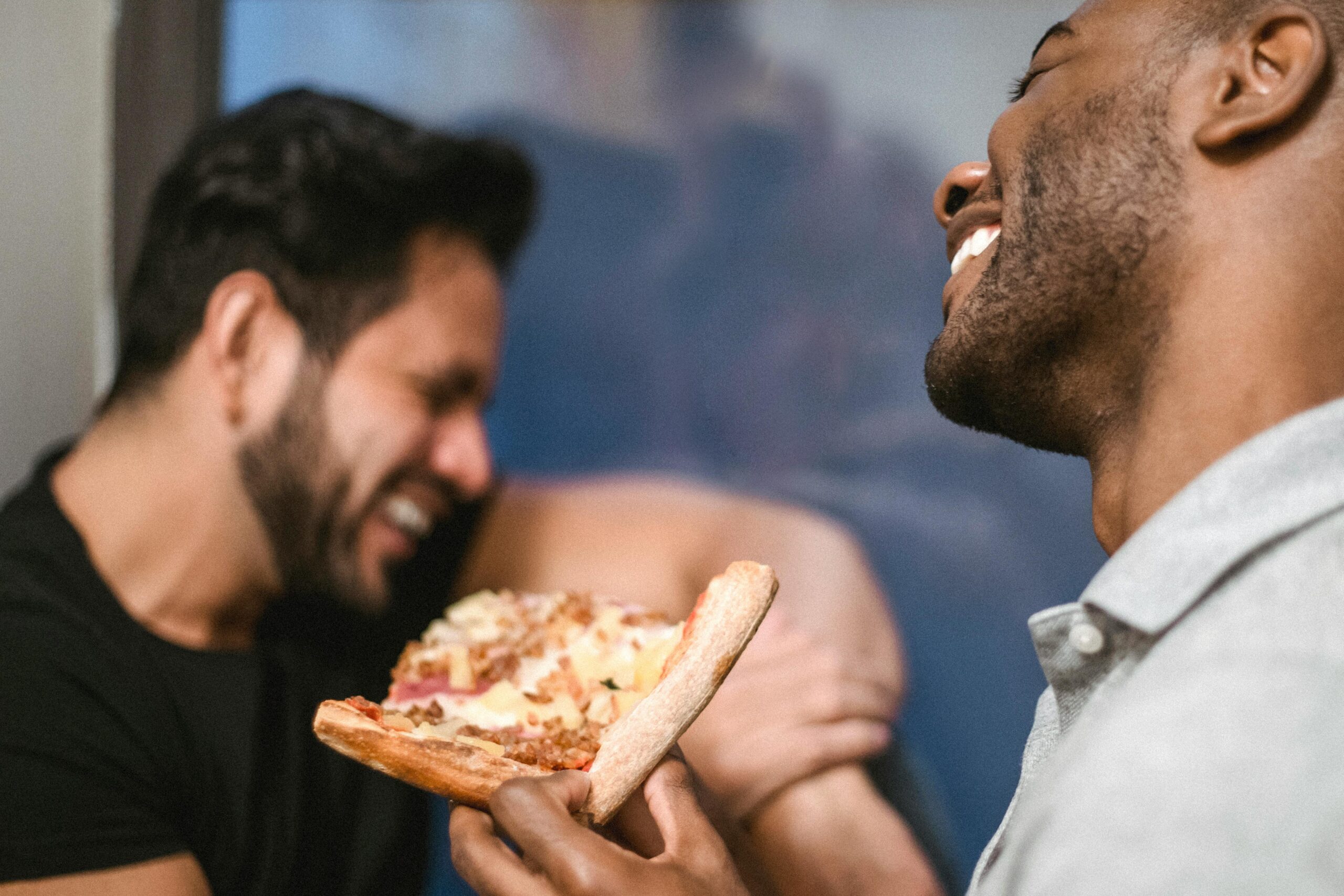 Two friends sharing a laugh while enjoying delicious pizza indoors, creating a joyful moment.