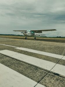 Small light aircraft standing on a tarmac runway with a cloudy sky backdrop.